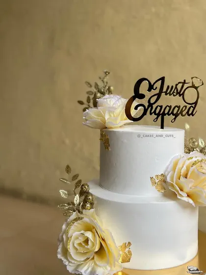 A beautiful two-tier cake for a "Just Engaged" celebration. This design features delicate white flowers with golden accents, creating a simple yet stunning look.