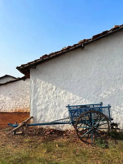A traditional blue bullock cart rests against the white wall of a village house. This simple scene offers a glimpse into the rural lifestyle that surrounds the historic site of Hampi.
