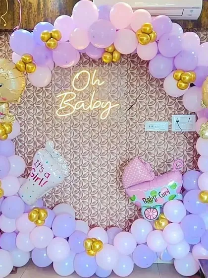 A lovely "Oh Baby" shower decoration for a baby girl. The balloon arch in shades of lavender and pink is accented with gold balloons and themed foils like a baby carriage.