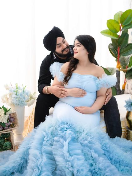 A sweet and intimate moment. The couple shares a look of love as they sit together, surrounded by soft blue florals that complement her beautiful ruffled gown.