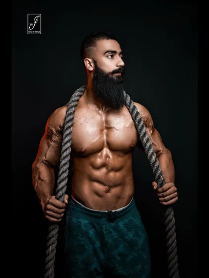A variation of the battle rope series, this pose captures a moment of calm intensity. The prop frames the upper body, drawing attention to the impressive chest and shoulder development.