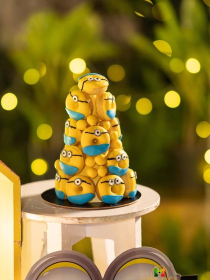 A tower of Minion-themed treats against a beautiful bokeh background. Themed desserts are a fantastic way to enhance the party's decor and delight the guests.