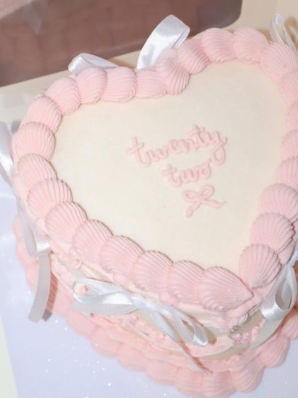 Twenty-two never looked so sweet. This heart-shaped cake features soft pink shell piping and is tied with delicate white ribbons for a classic and pretty birthday look.
