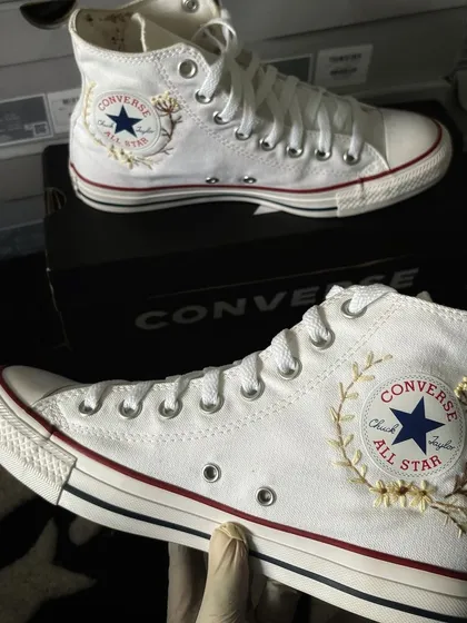 The embroidered Converse held up, showcasing the detailed threadwork.