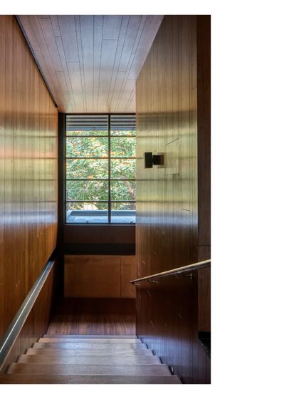A wooden staircase at the Lakeshore house, where the warm tones of the paneling are illuminated by light from a high window. Build quality, craft, and material are the tools that turn building into art.