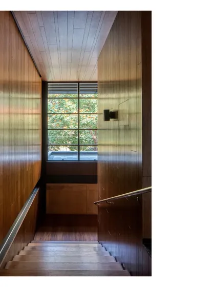 A staircase at the Lakeshore house, paneled in wood. The light from the window highlights the grain of the wood and the clean lines of the construction, showing how details make architecture.