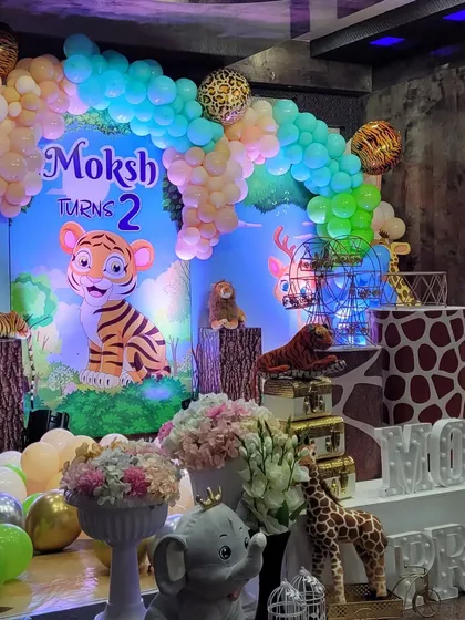 A close-up of the jungle party stage, showing the mix of floral arrangements, stuffed animals, and themed props like vintage suitcases and birdcages to create a rich, layered look.