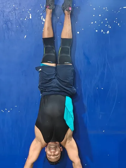 A smiling athlete holds a handstand against the wall, building shoulder strength and getting comfortable being upside down.