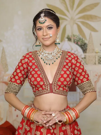 A full portrait of a stunning bride in her red lehenga. The makeup is designed to enhance her features, with a focus on glowing skin and expressive eyes, making her look and feel like royalty.