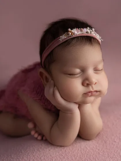 An adorable 'chin on hands' pose in a pink outfit. This pose is a client favorite and beautifully showcases the baby's sweet face.
