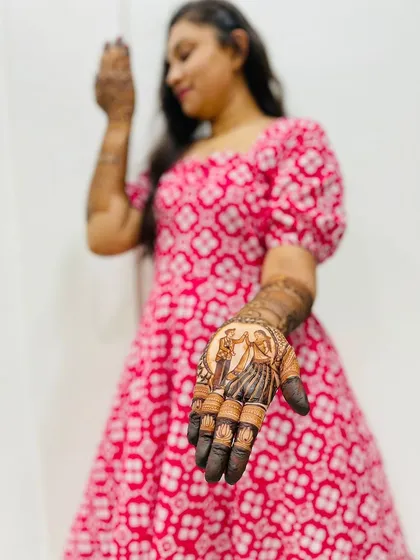 A bride showcasing her custom mehndi, which features a portrait of the couple on her palm.