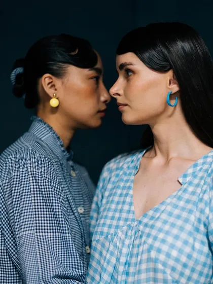 An intimate nose-to-nose portrait for Label Rama. The shot highlights the models' profiles and the contrast between their gingham shirts and colorful earrings.