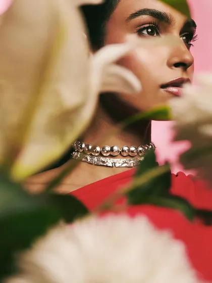 An artistic close-up of the silver choker, framed by out-of-focus flowers. This composition creates a soft, romantic feel while still highlighting the jewelry.
