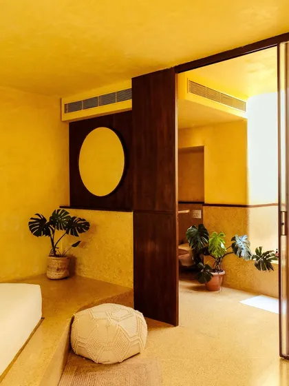 The interior of a suite, showing how the bedroom and bathroom spaces are divided by rich, dark wood panels and decorated with indoor plants.