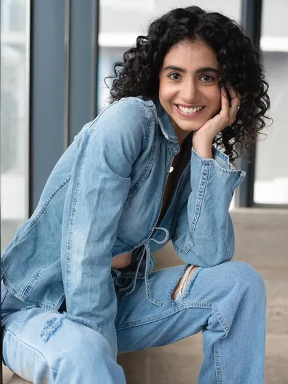 A smiling shot of a model with natural curls in a denim outfit. The makeup is subtle, designed to look like her own skin but better, perfect for a commercial or lifestyle photoshoot.