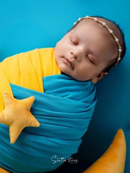 A close-up of a newborn wrapped in blue and yellow, resting on a moon prop with a little star.