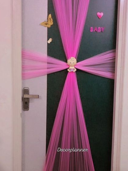 A creative and elegant door decoration for a baby's room. I used pink tulle to create a beautiful wrap-around effect, centered with a small baby doll, to announce the arrival of the little one.
