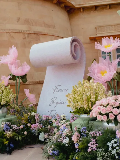 A personalized scroll that reads "Forever Begins Today," set within a garden of oversized pink lotuses and pastel florals, creating a whimsical and romantic photo opportunity.
