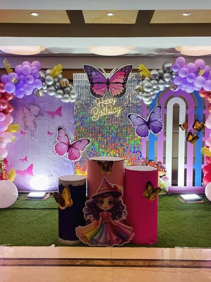 A colorful butterfly theme for a first birthday, featuring a shimmer wall, large butterfly cutouts, and a balloon garland in purple and pink.
