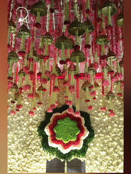 A close-up of the floral backdrop, showing the intricate work of the floral 'rangoli' and the hanging temple bells and flower tassels.
