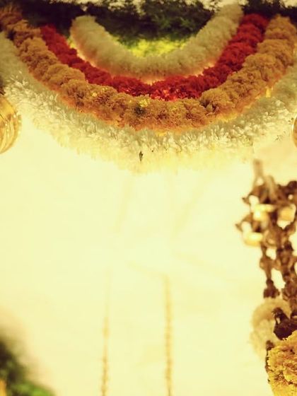 A detail shot of the hanging brass 'kumbah' elements. These traditional pieces add a touch of heritage and shine, perfectly complementing the colorful floral garlands in our desi decor setups.