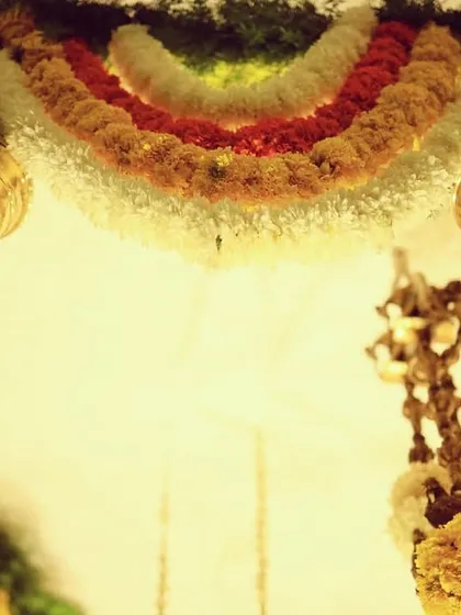 A detail shot of the hanging brass 'kumbah' elements. These traditional pieces add a touch of heritage and shine, perfectly complementing the colorful floral garlands in our desi decor setups.