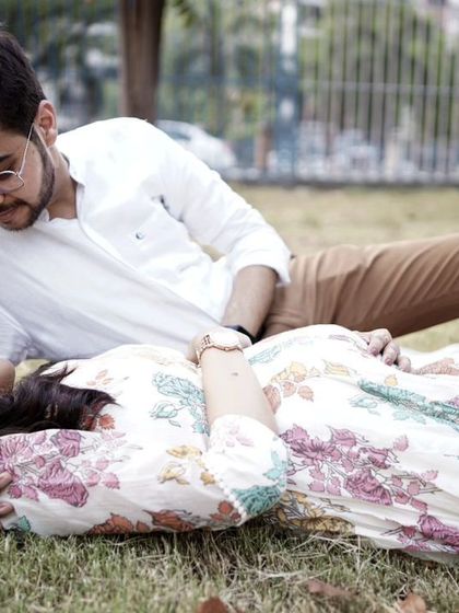 A relaxed and romantic pose for an outdoor maternity session. The couple lies on the grass in a park, sharing a tender moment as they await their new arrival.
