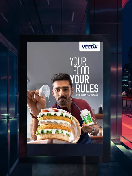 This Veeba Mayonnaise ad, shown in a nighttime bus stop mockup, features a massive, multi-layered burger. The dramatic lighting and scale are designed to make the product look indulgent and aspirational.