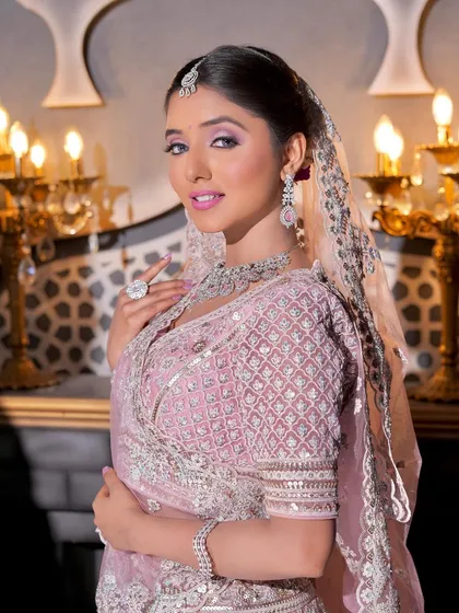 A beautiful bride looking gorgeous for her wedding in a regal pink lehenga. The makeup is glamorous, with a focus on dramatic eyes and luminous skin, set against an opulent backdrop.