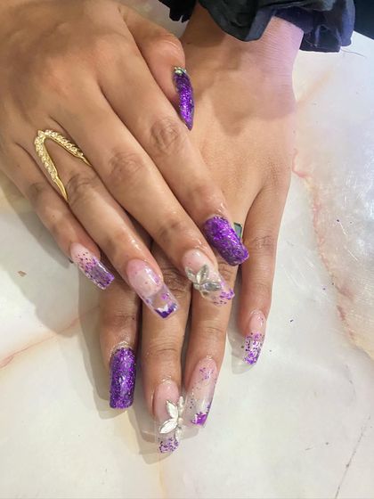 A bold and glamorous set featuring a deep purple glitter ombré on a clear base. The design is enhanced with delicate, sculpted 3D flowers, showing skill in both glitter application and dimensional art.