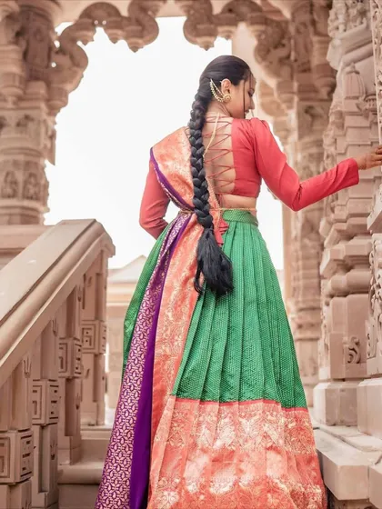 I love to blend tradition with a touch of modern style. This Langa Dhavani features a unique corset-style back on the blouse, adding a contemporary twist to a classic South Indian silhouette. The combination of green, red, and orange is just so full of life.