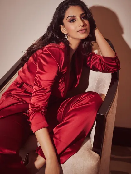 A relaxed yet poised seated pose in the red satin pantsuit. This shows the versatility of the outfit, looking just as chic in a candid moment.