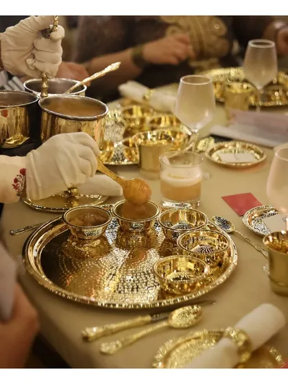 We honour India's rich culinary legacy with our traditional silver service. This image showcases an elaborate sit down feast, where guests are served from magnificent hammered brass and silver thalis, reflecting a timeless elegance and a truly royal dining experience.