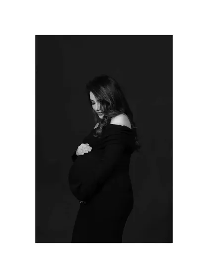 A contemplative black and white portrait. The mother-to-be cradles her bump, her expression soft and thoughtful, in this beautifully lit, low-key studio shot.