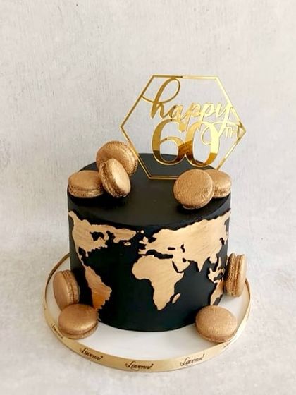 A chic black and gold cake for a 60th birthday. The cake features a gold world map and is topped with matching gold macarons.
