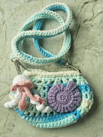 The back view of the mini Ocean Bag, highlighting the purple seashell and the dangling jellyfish charm. Every part of this bag is crocheted and assembled by hand with lots of care.