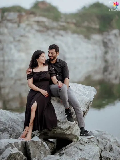 A classic portrait of a couple in matching black outfits, sitting on a rock by the water, exuding a cool and confident vibe.