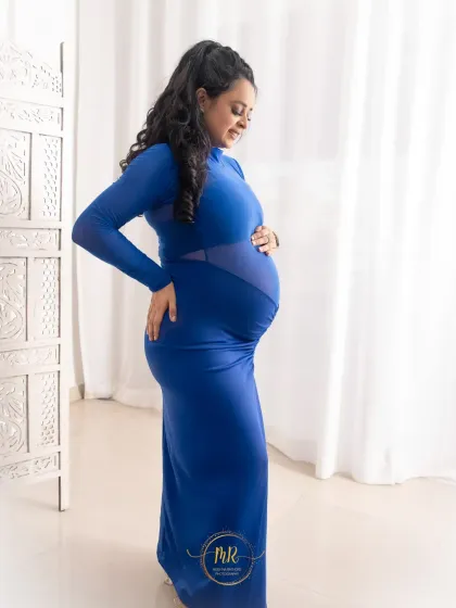 A side-profile maternity portrait in a form-fitting royal blue gown. The sheer panels add a modern touch, and the bright studio lighting creates a fresh and clean look.