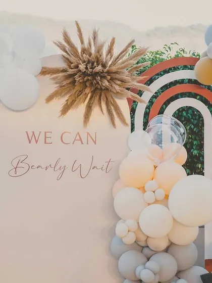 The main photo backdrop for the 'We Can Bearly Wait' baby shower, featuring pastel balloons, pampas grass, and a cute teddy bear on a peacock chair.