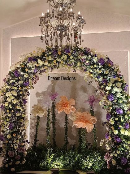 A full view of a stunning photo backdrop. A grand floral arch is accented by a crystal chandelier hanging from the center, creating a look of pure elegance and sophistication.
