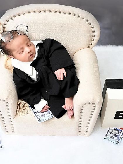 The Boss Baby is in charge. This humorous and creative setup features a newborn in a suit, surrounded by money and a 'Boss' briefcase.