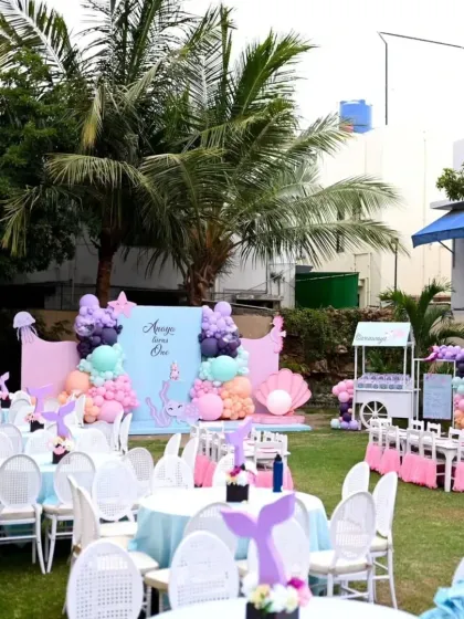 The full outdoor setup for the 'Under the Sea' party, with themed table centerpieces, a dessert cart, and a beautiful backdrop set against a lush green lawn.