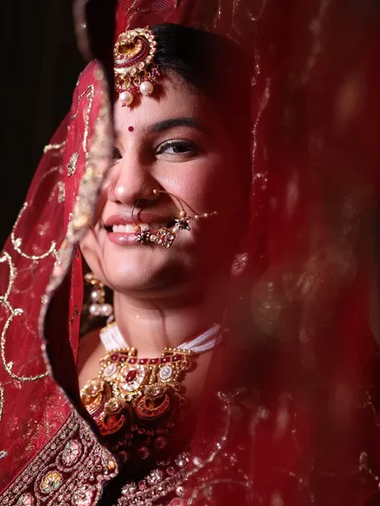 A peek through the veil. This artistic shot captures the bride's happy smile and the flawless finish of her makeup, even under the traditional red dupatta.