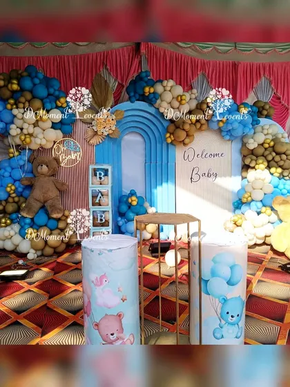 Another view of the baby welcome stage, showing the themed pedestals and a large teddy bear prop, all in a coordinated blue and brown color scheme.