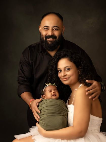 A classic family portrait with a newborn. The parents smile proudly as they hold their new baby, who is safely swaddled and resting in her mother's arms.