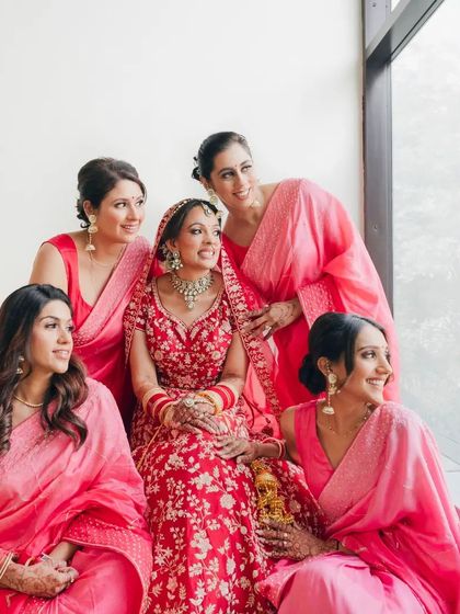 A beautiful portrait of the bride with her bridesmaids, all dressed in shades of pink and red, smiling brightly.