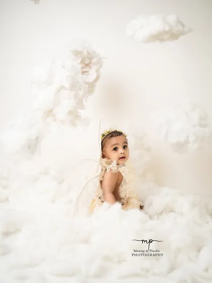 An angel peeking out from behind the clouds. The all-white theme creates a pure and serene atmosphere for these beautiful milestone photos.