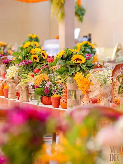 A close-up of the tablescape, featuring a vibrant mix of sunflowers, marigolds, and other seasonal blooms in terracotta pots and burlap-wrapped vases. Every detail was chosen to enhance the rustic, earthy feel.