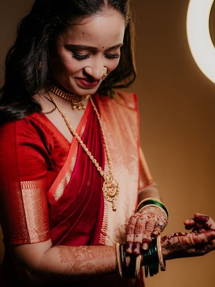 A beautiful getting-ready shot of the bride, Sonali, as she puts on her traditional green bangles, her red saree vibrant against the warm light.