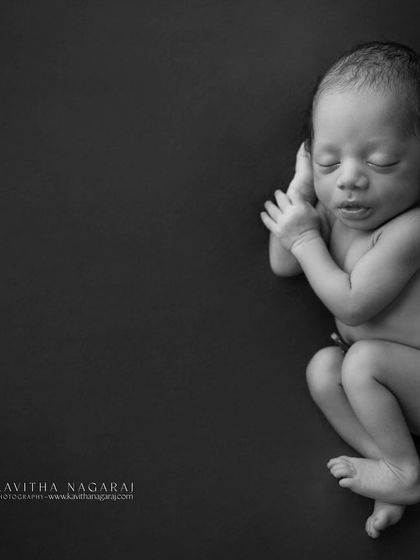 A newborn in a dramatic black and white portrait. The dark background makes the baby's form stand out, creating a powerful and artistic image.